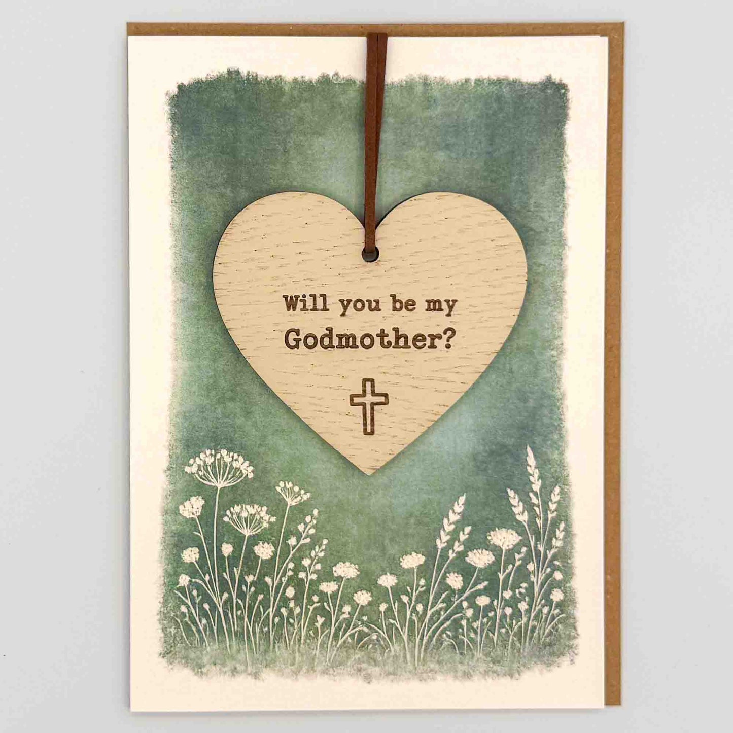 Godmother proposal cross heart keepsake card from Sprinkled with Magic, featuring a removable wooden heart keepsake, small cross detail, green botanical design and recycled kraft envelope.