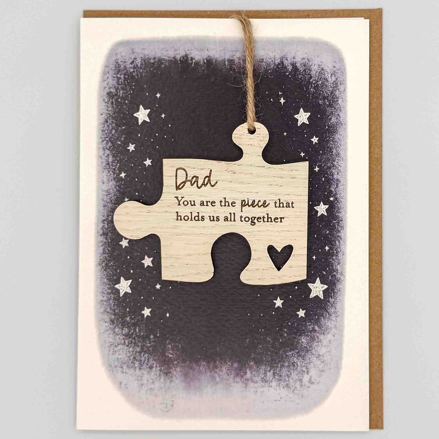 Dad hold us together jigsaw keepsake card from Sprinkled with Magic, featuring a removable wooden jigsaw keepsake, small heart detail, starry navy design and recycled kraft envelope.