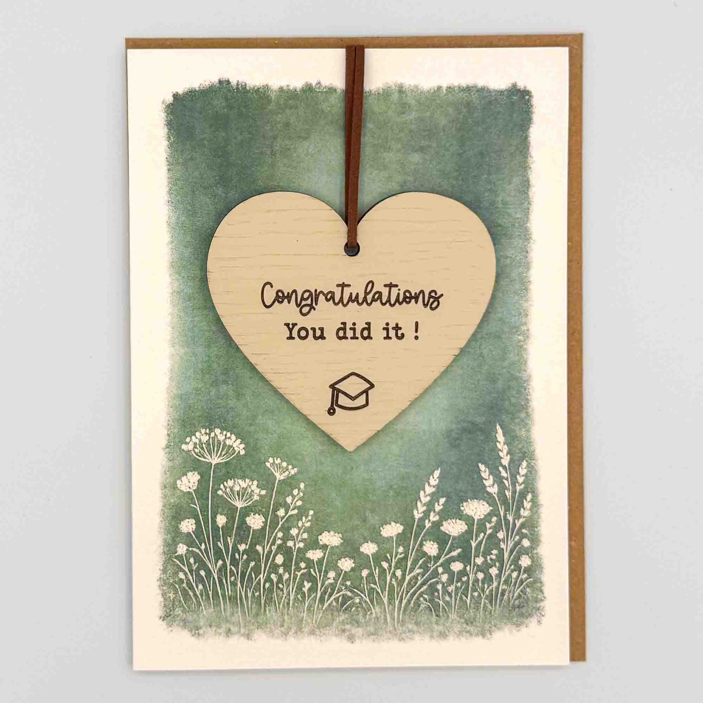 Congratulations graduation cap heart keepsake card from Sprinkled with Magic, featuring a removable wooden heart keepsake, graduation cap detail, green botanical design and recycled kraft envelope.