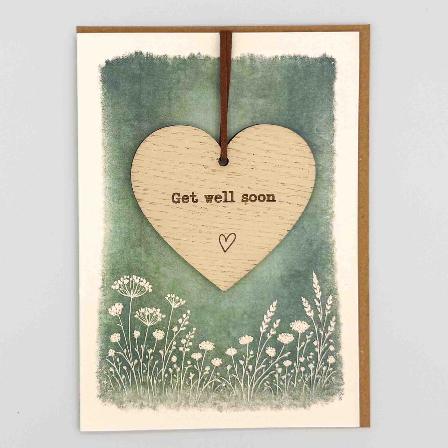 Get well soon heart keepsake card from Sprinkled with Magic, featuring a removable wooden heart keepsake, small heart detail, green botanical design and recycled kraft envelope.