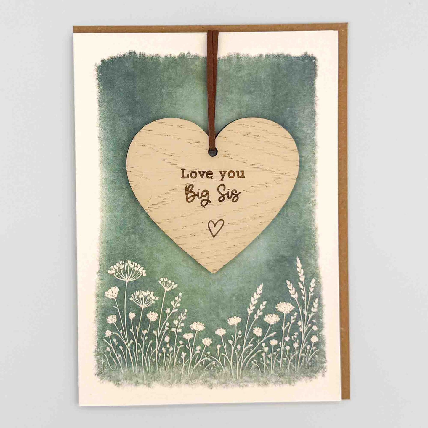 Love you big sis heart keepsake card from Sprinkled with Magic, featuring a removable wooden heart keepsake, green botanical design and recycled kraft envelope.
