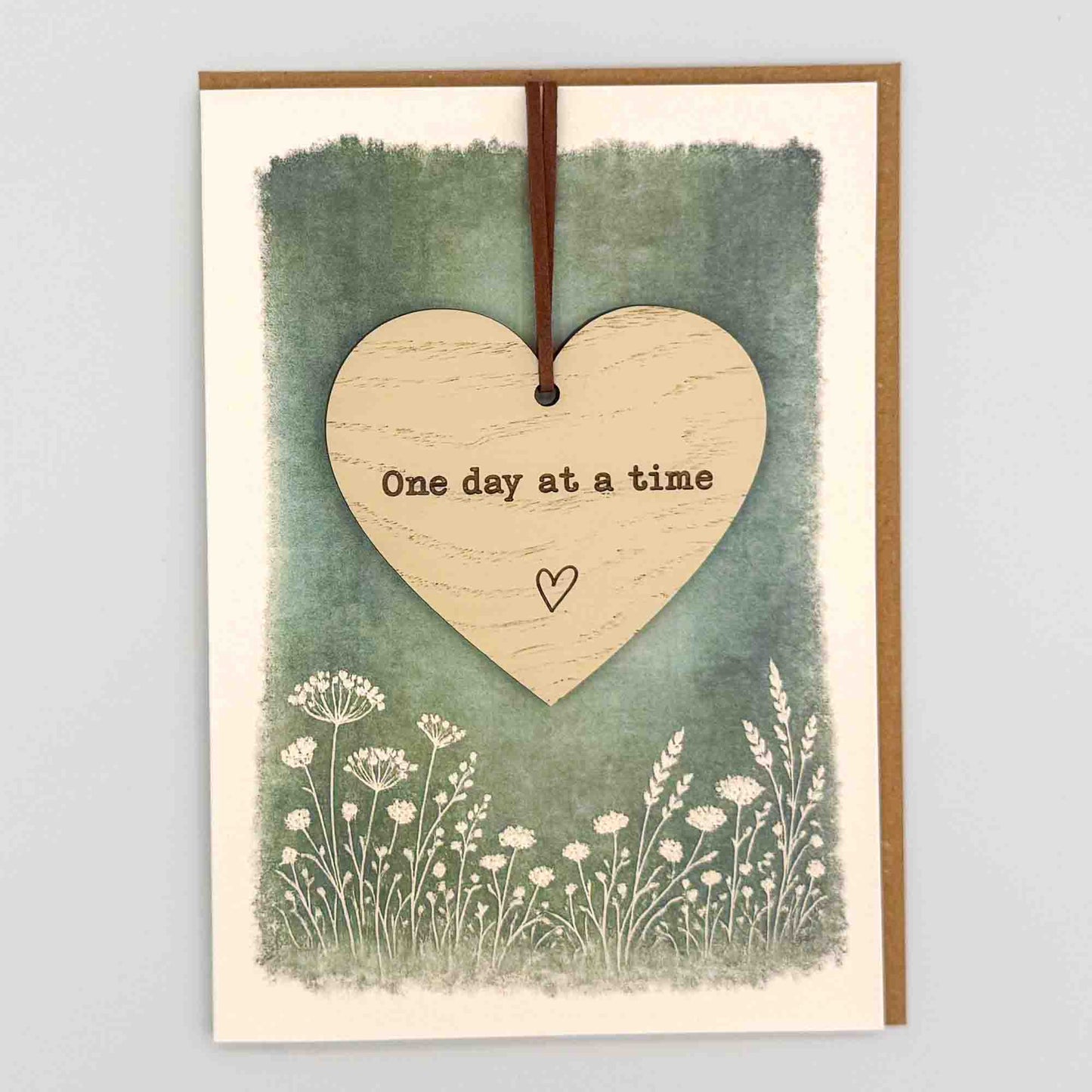 One day at a time heart keepsake card from Sprinkled with Magic, featuring a removable wooden heart keepsake, green botanical design and recycled kraft envelope.