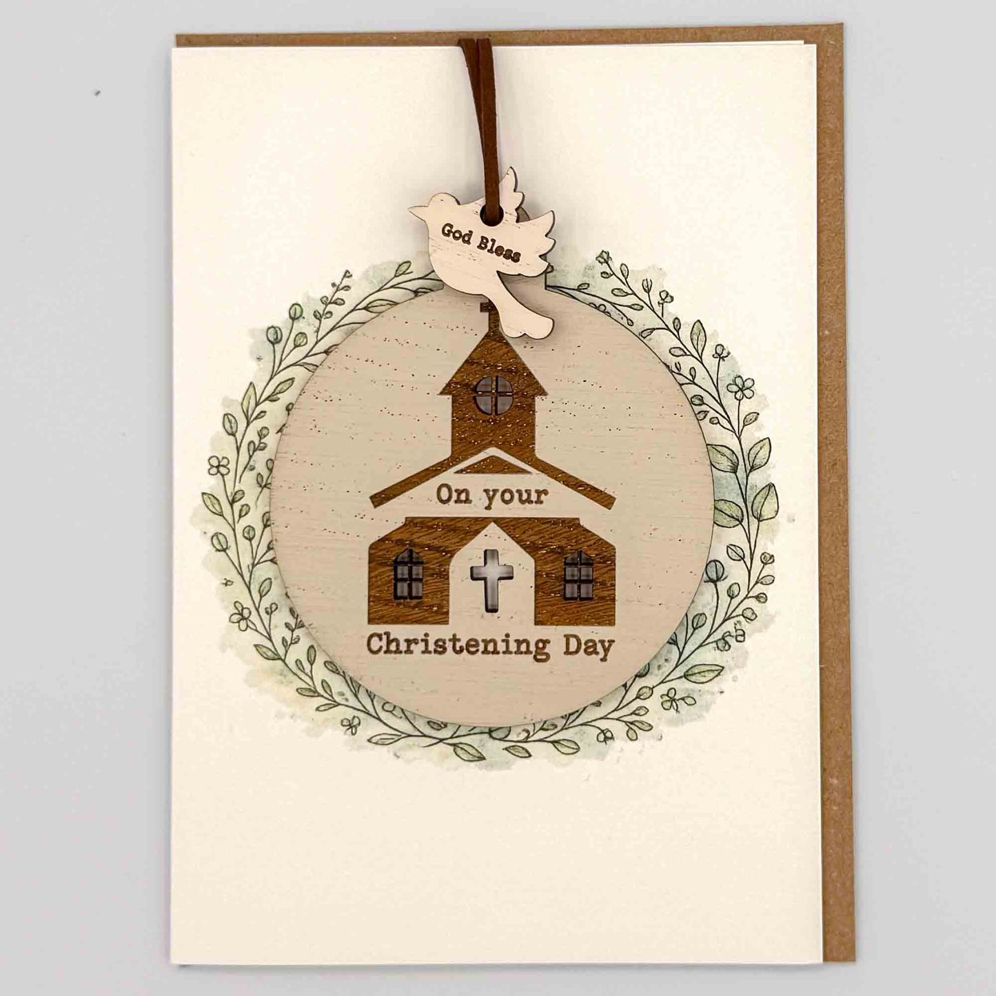 Christening Day church bauble keepsake card from Sprinkled with Magic, featuring a removable wooden church bauble keepsake, cross detail, leafy wreath design and recycled kraft envelope.