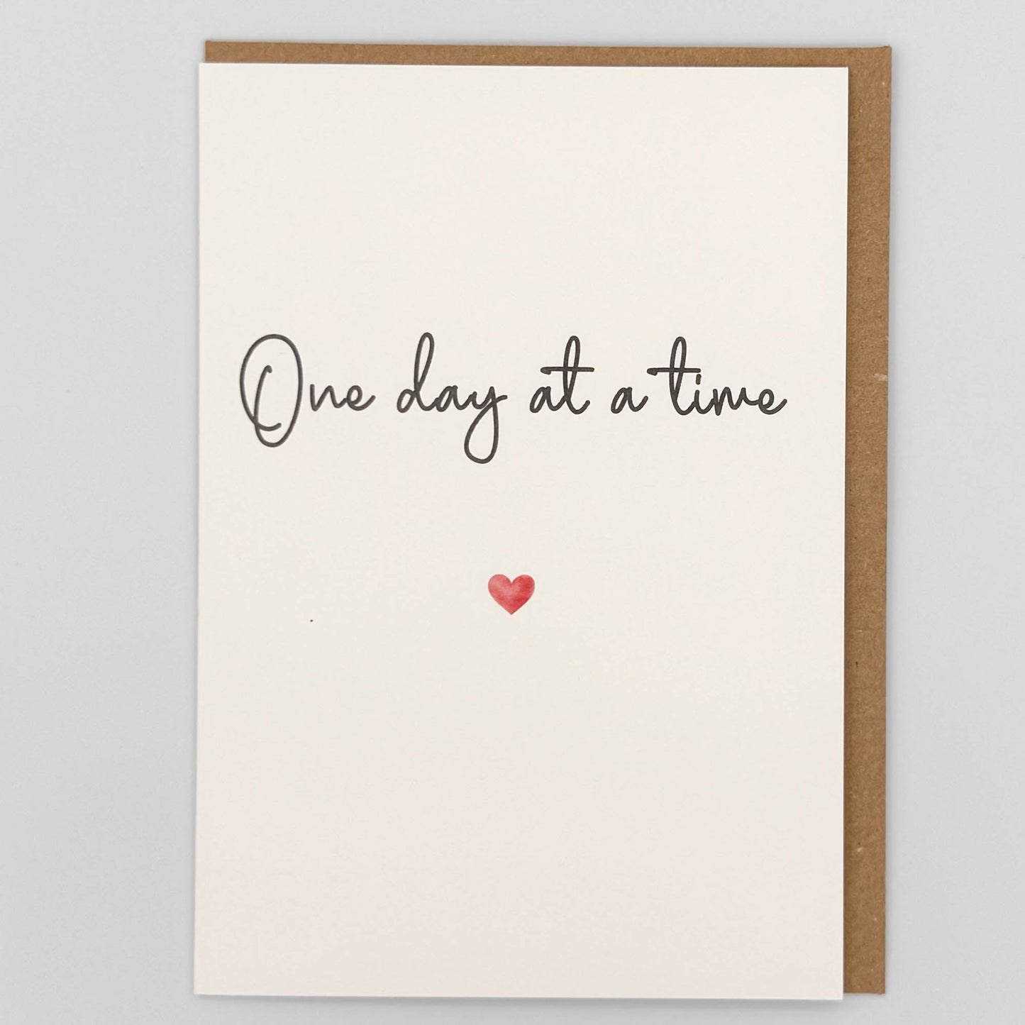 One day at a time card from Sprinkled with Magic, featuring handwritten-style reassurance wording, a small red heart and recycled kraft envelope.