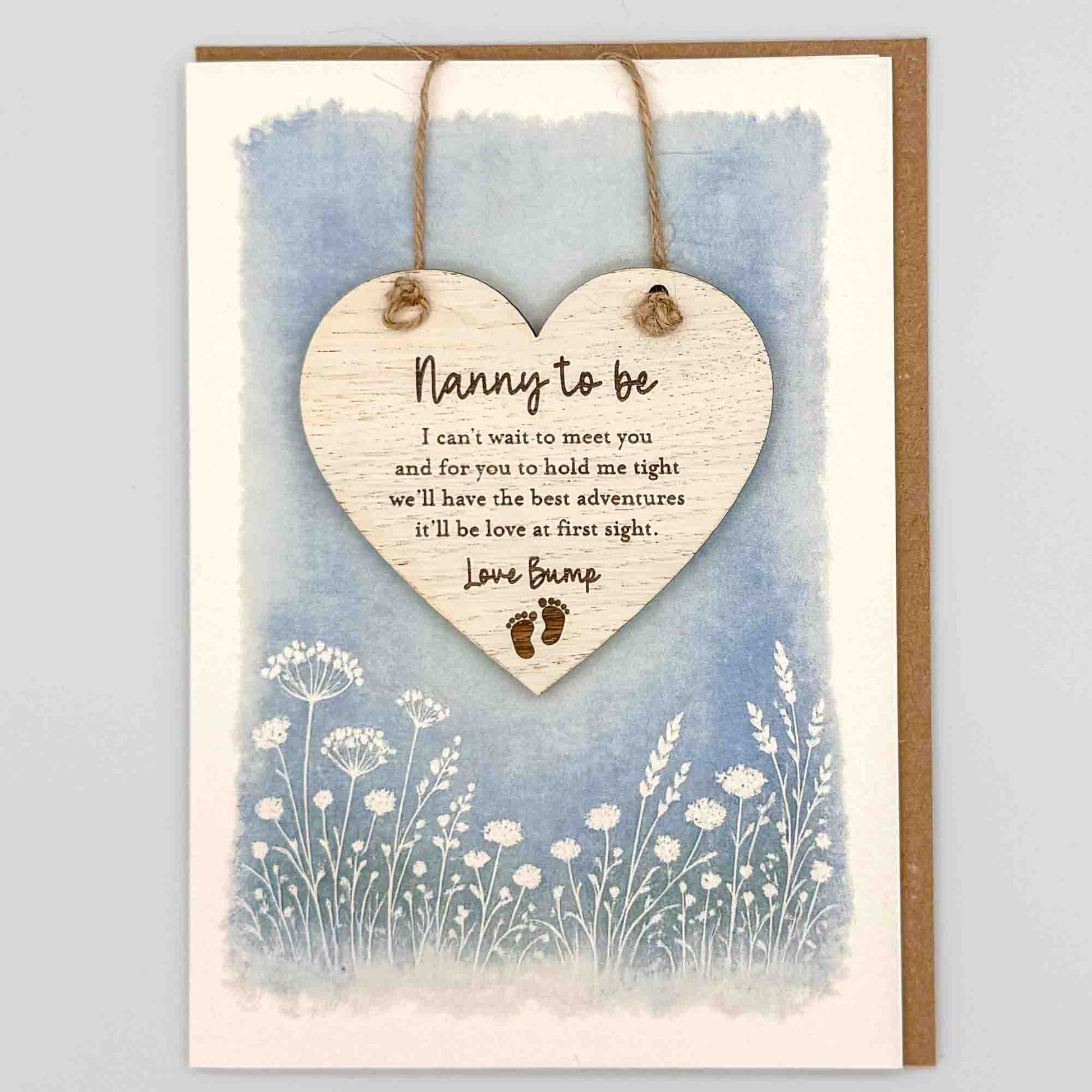 Nanny to be love bump heart keepsake card from Sprinkled with Magic, featuring a removable wooden heart keepsake, baby feet detail, blue botanical design and recycled kraft envelope.