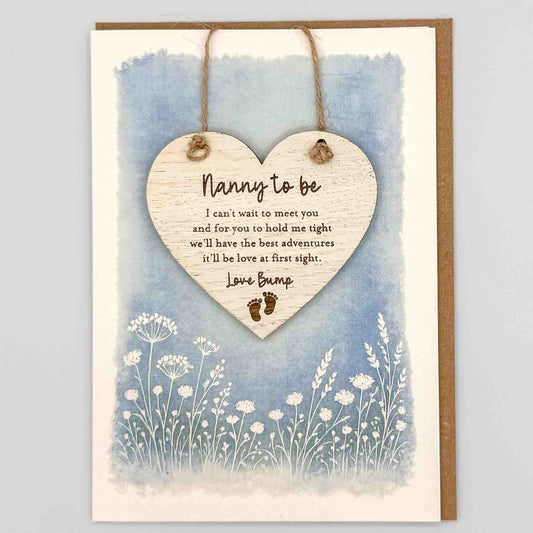 Nanny to be love bump heart keepsake card from Sprinkled with Magic, featuring a removable wooden heart keepsake, baby feet detail, blue botanical design and recycled kraft envelope.
