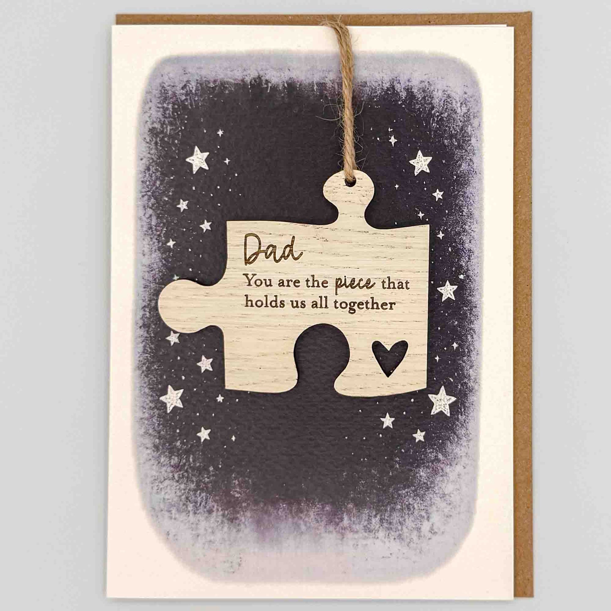 Dad hold us together jigsaw keepsake card from Sprinkled with Magic, featuring a removable wooden jigsaw keepsake, small heart detail, starry navy design and recycled kraft envelope.