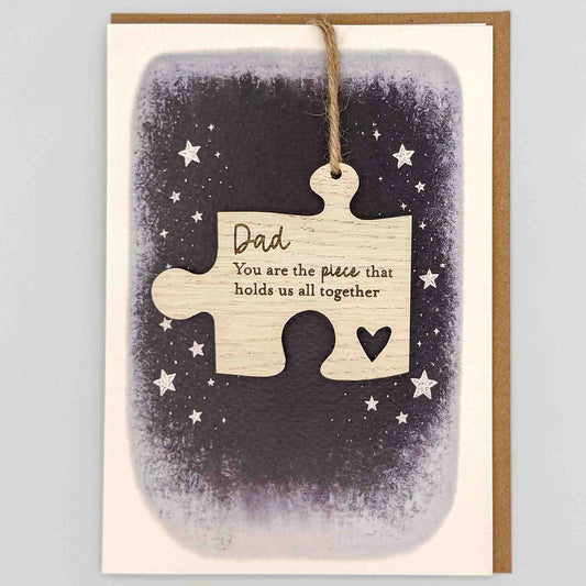 Dad hold us together jigsaw keepsake card from Sprinkled with Magic, featuring a removable wooden jigsaw keepsake, small heart detail, starry navy design and recycled kraft envelope.