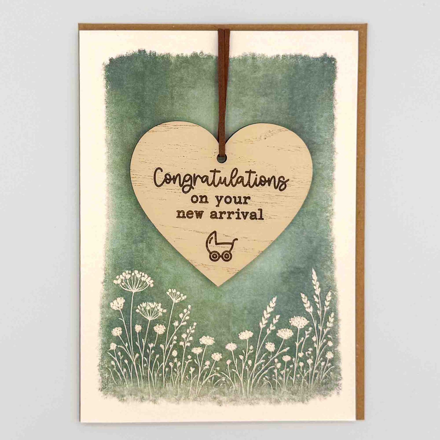 Congratulations new arrival pram heart keepsake card from Sprinkled with Magic, featuring a removable wooden heart keepsake, small pram detail, green botanical design and recycled kraft envelope.