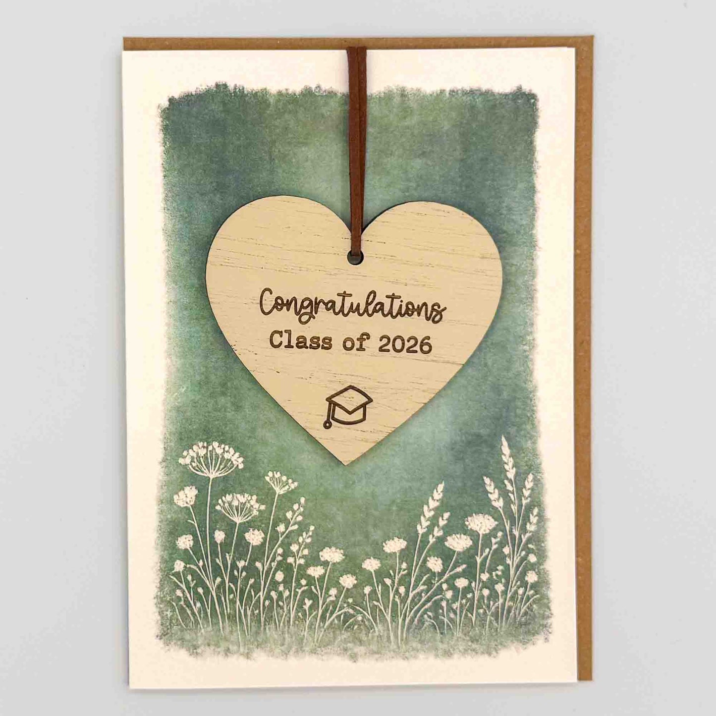 Congratulations Class of 2026 graduation heart keepsake card from Sprinkled with Magic, featuring a removable wooden heart keepsake, graduation cap detail, green botanical design and recycled kraft envelope.