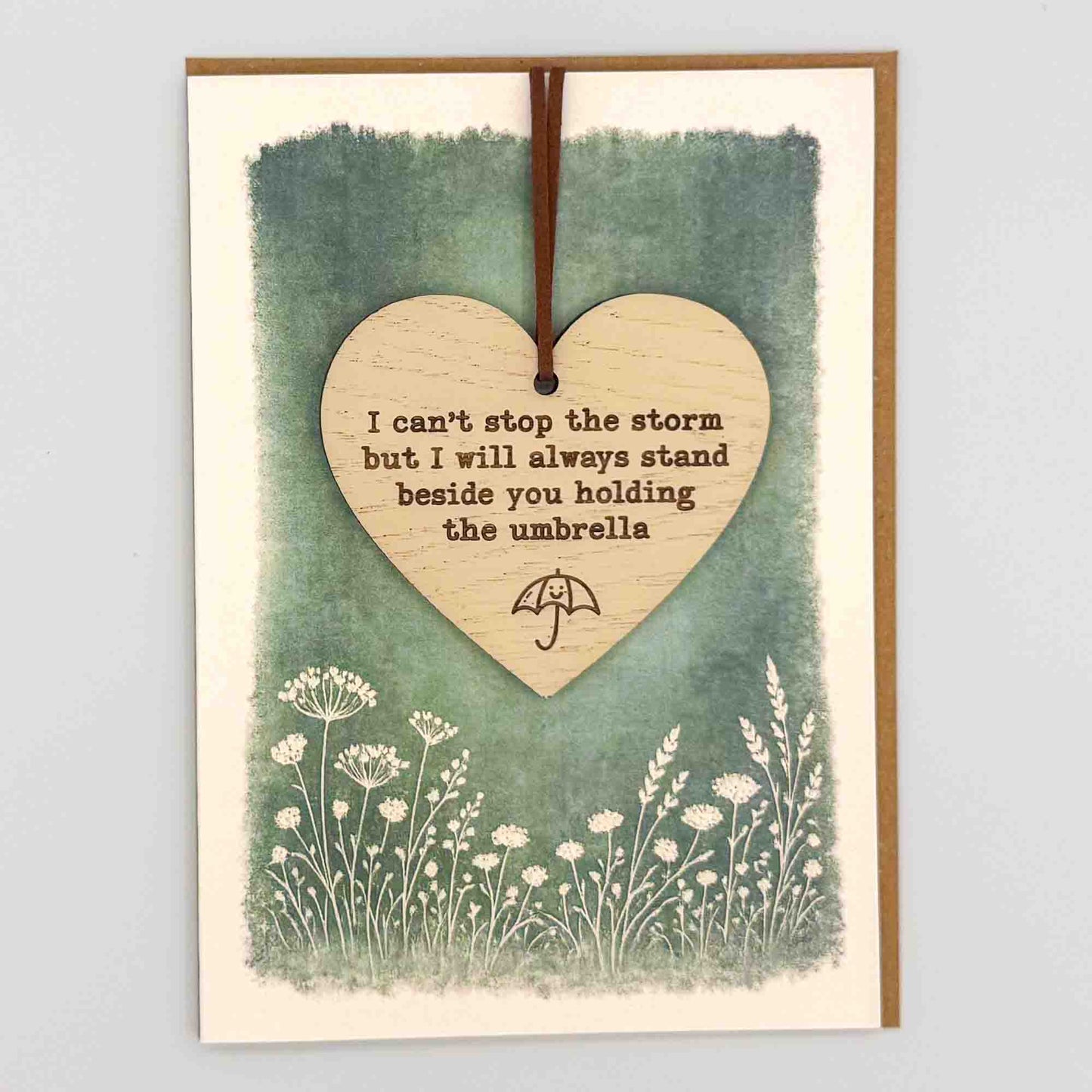 Can’t stop the storm umbrella heart keepsake card from Sprinkled with Magic, featuring a removable wooden heart keepsake, small umbrella detail, green botanical design and recycled kraft envelope.