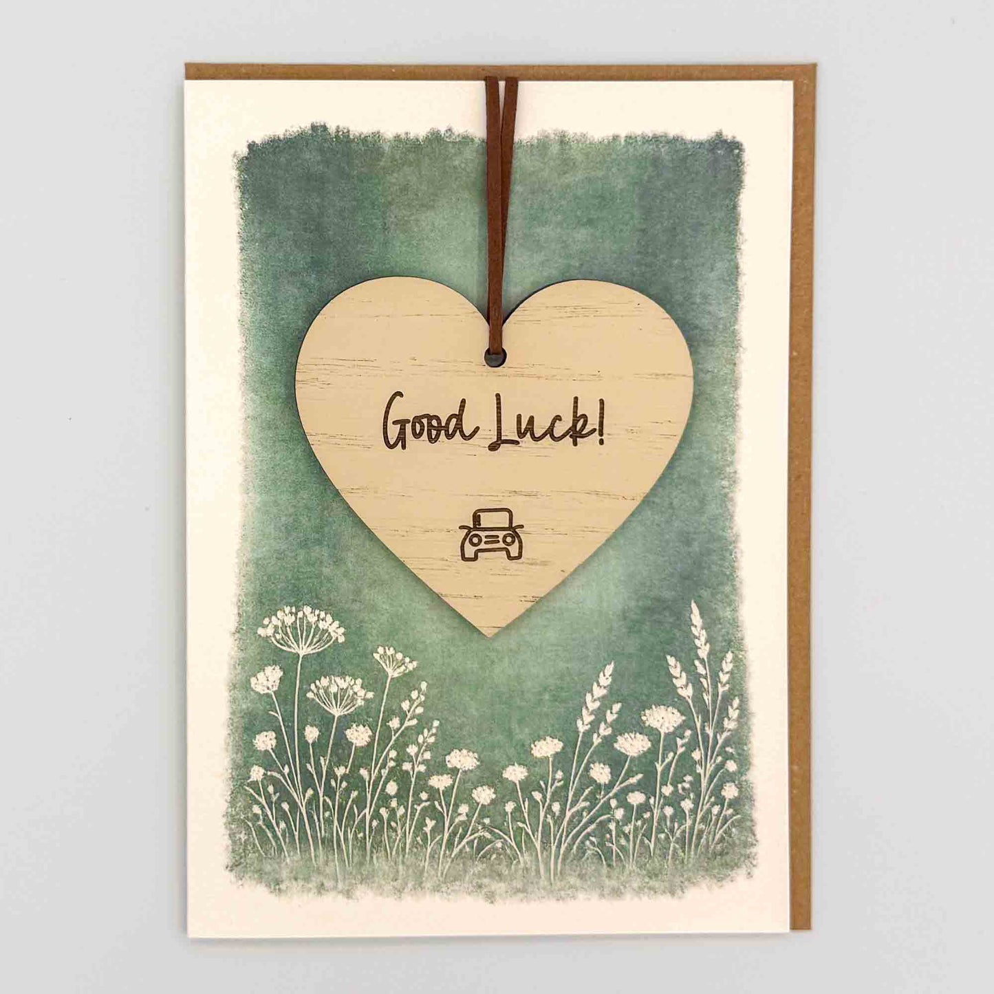 Good luck car heart keepsake card from Sprinkled with Magic, featuring a removable wooden heart keepsake, small car detail, green botanical design and recycled kraft envelope.