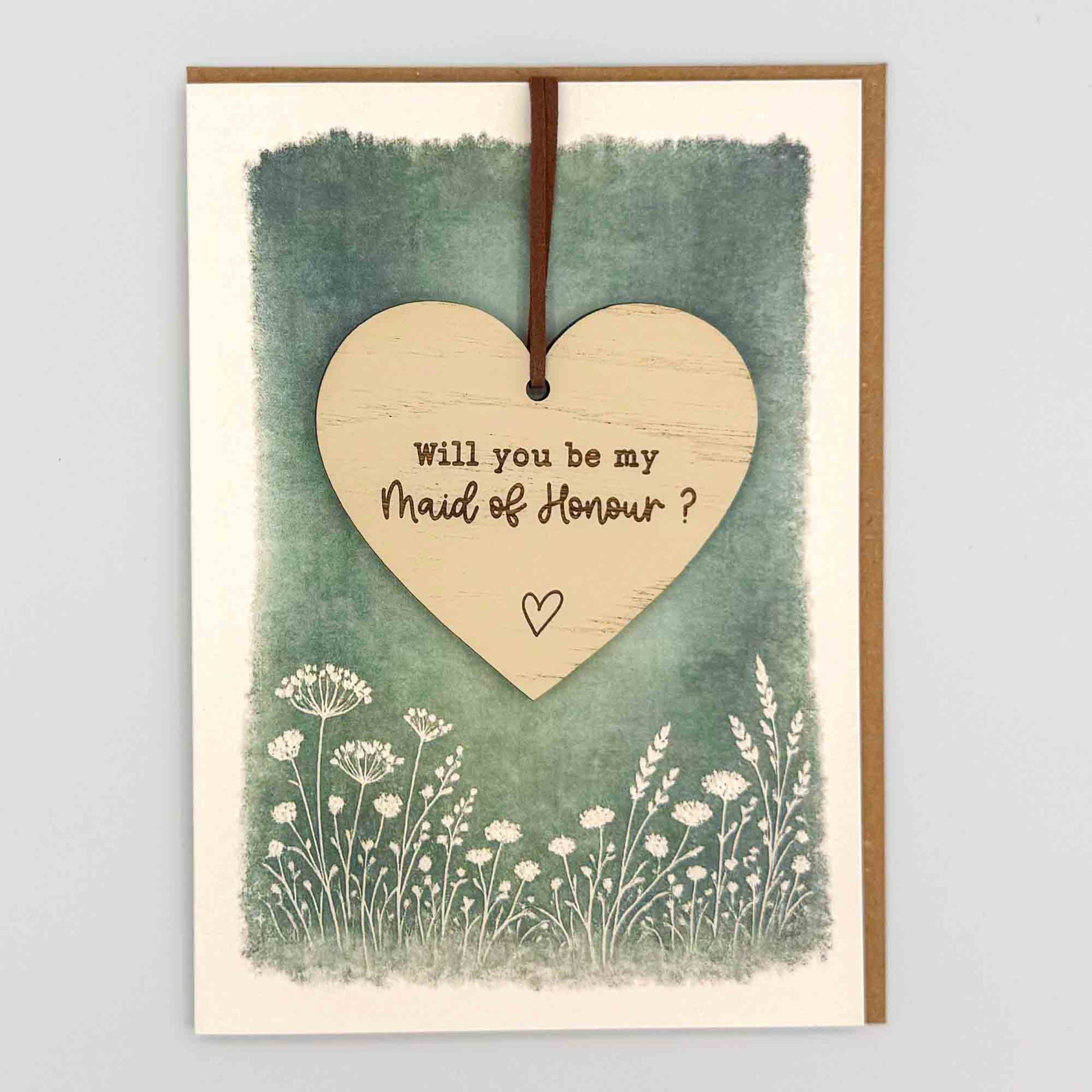 Maid of Honour proposal heart keepsake card from Sprinkled with Magic, featuring a removable wooden heart keepsake, small heart detail, green botanical design and recycled kraft envelope.