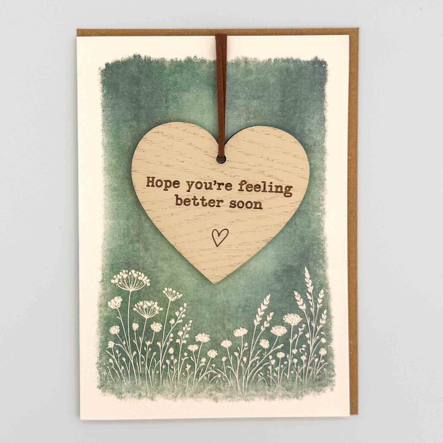 Feel better soon heart keepsake card from Sprinkled with Magic, featuring a removable wooden heart keepsake, small heart detail, green botanical design and recycled kraft envelope.