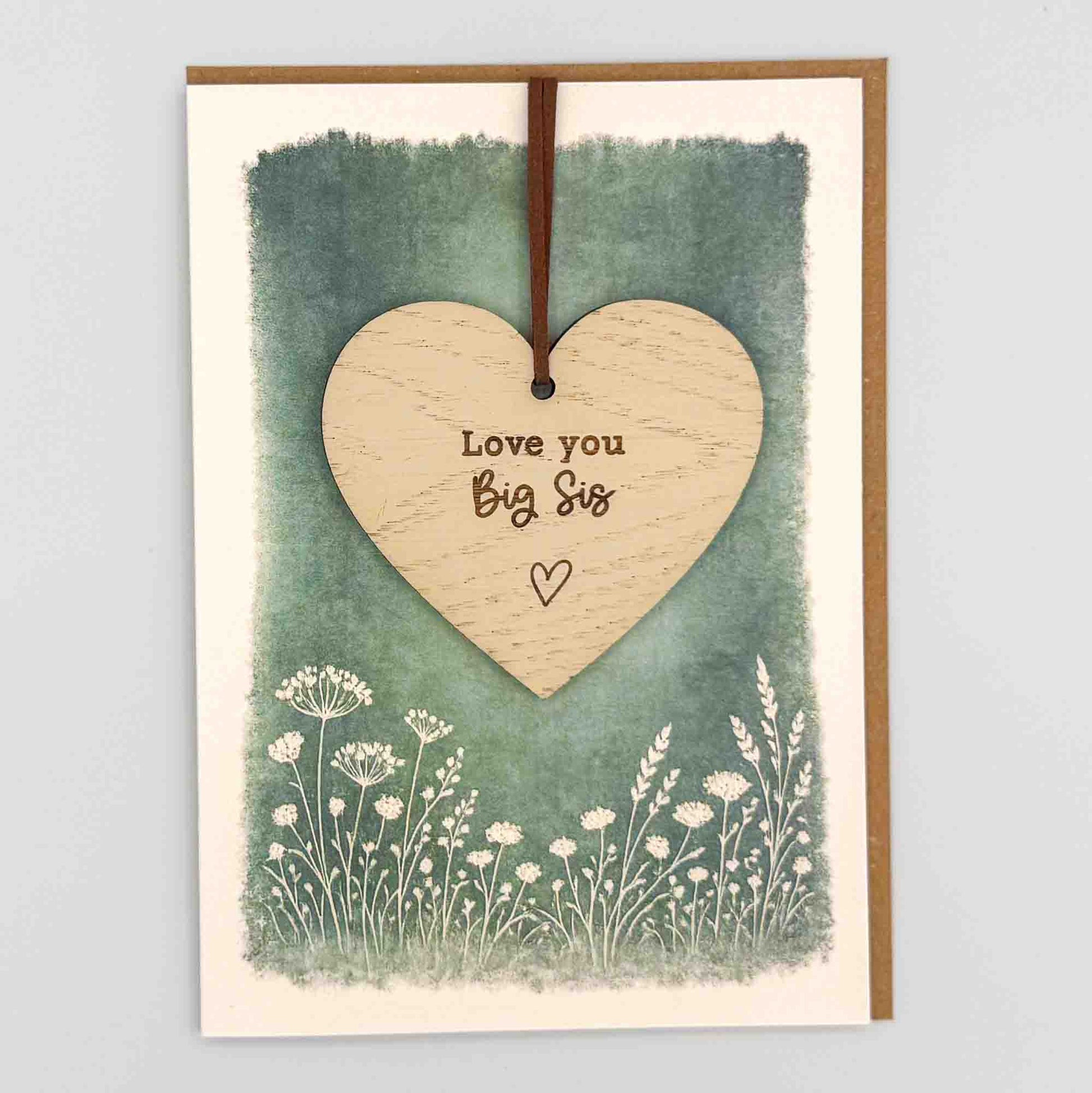 Love you big sis heart keepsake card from Sprinkled with Magic, featuring a removable wooden heart keepsake, green botanical design and recycled kraft envelope.