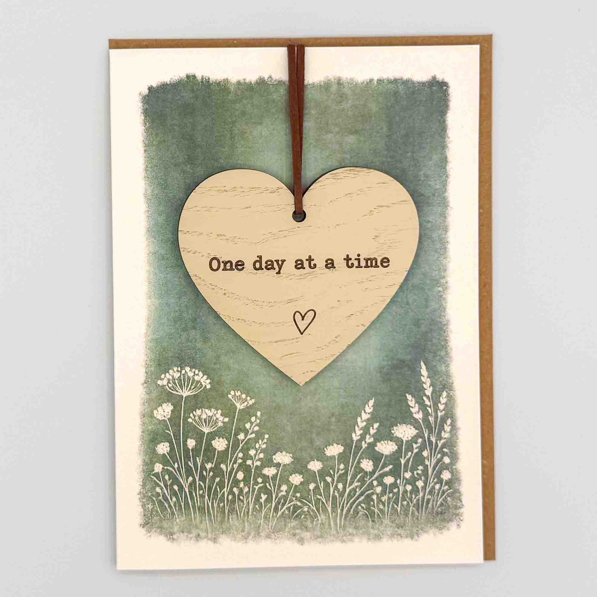 One day at a time heart keepsake card from Sprinkled with Magic, featuring a removable wooden heart keepsake, green botanical design and recycled kraft envelope.