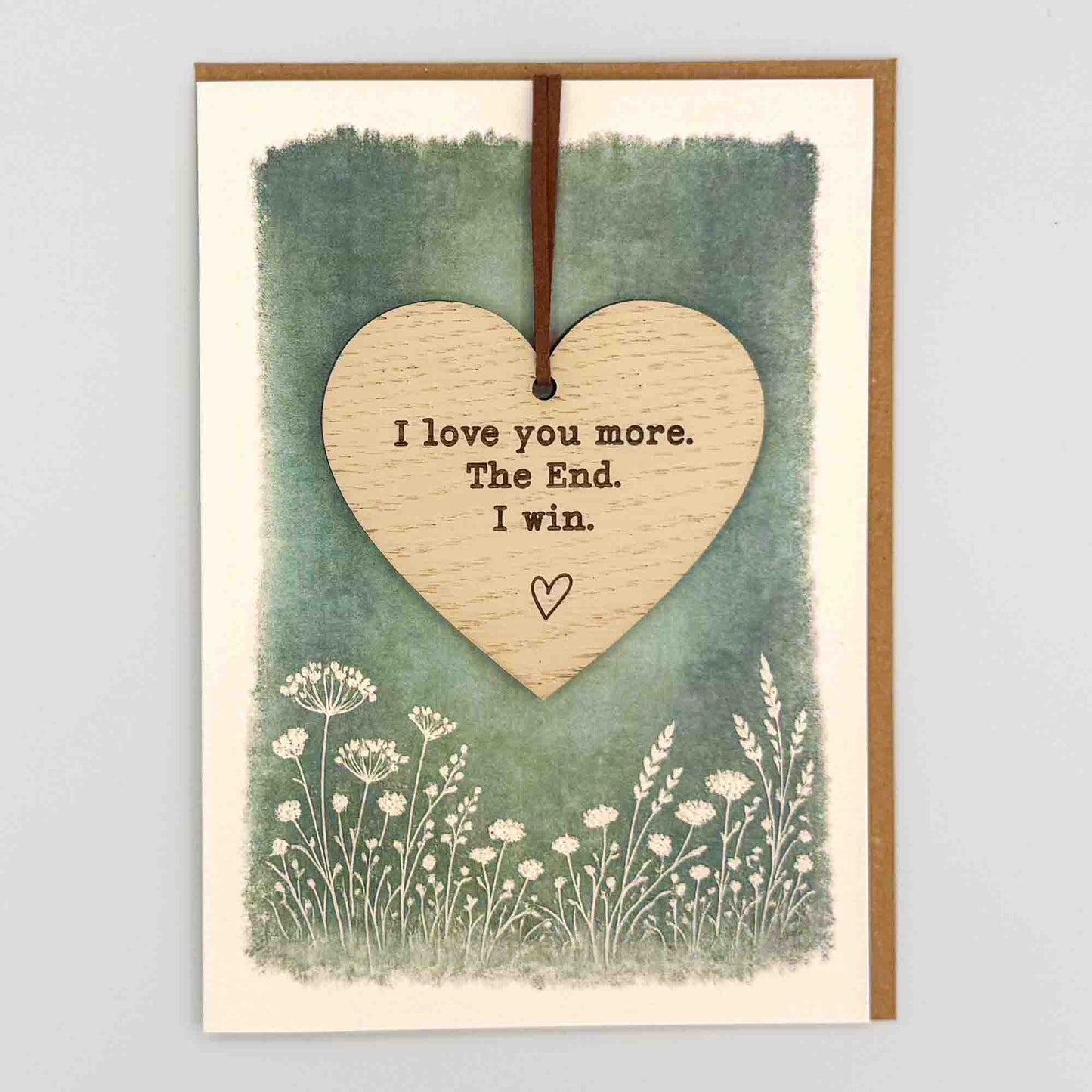 I love you more heart keepsake card from Sprinkled with Magic, featuring a removable wooden heart keepsake, green botanical design and recycled kraft envelope.