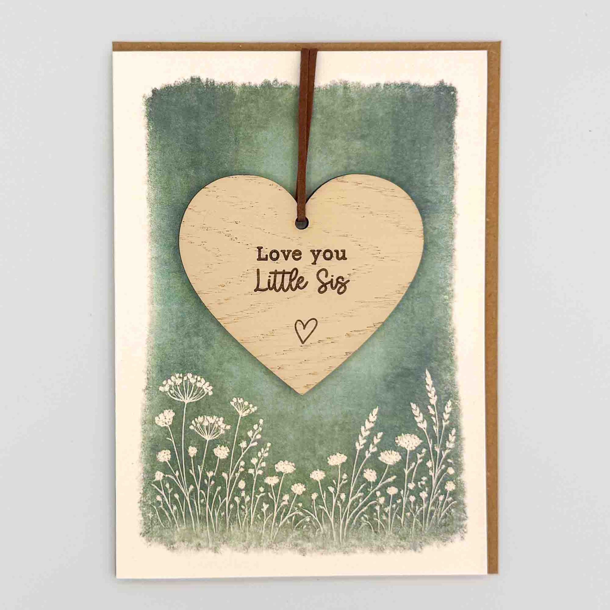 Love you little sis heart keepsake card from Sprinkled with Magic, featuring a removable wooden heart keepsake, green botanical design and recycled kraft envelope.