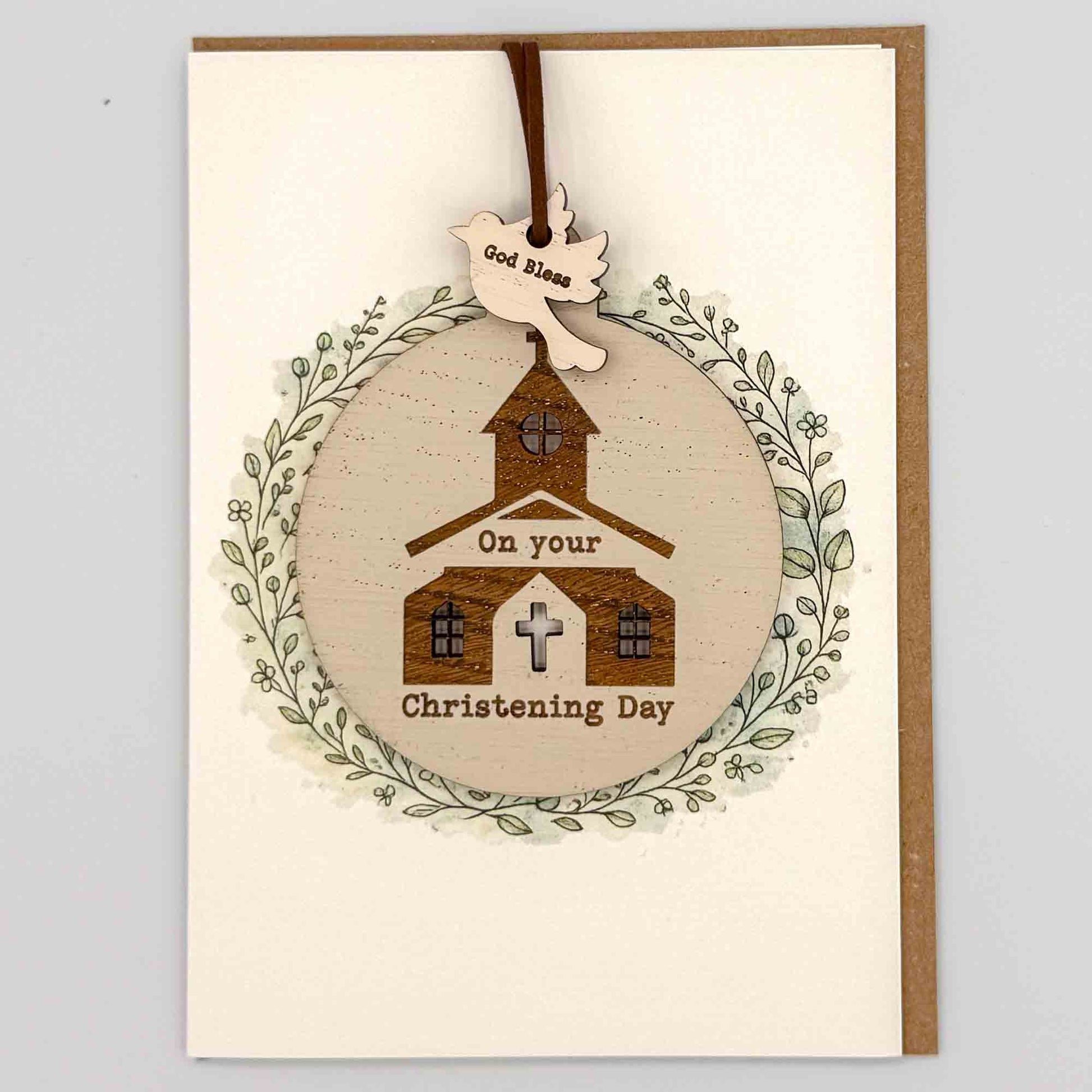 Christening Day church bauble keepsake card from Sprinkled with Magic, featuring a removable wooden church bauble keepsake, cross detail, leafy wreath design and recycled kraft envelope.