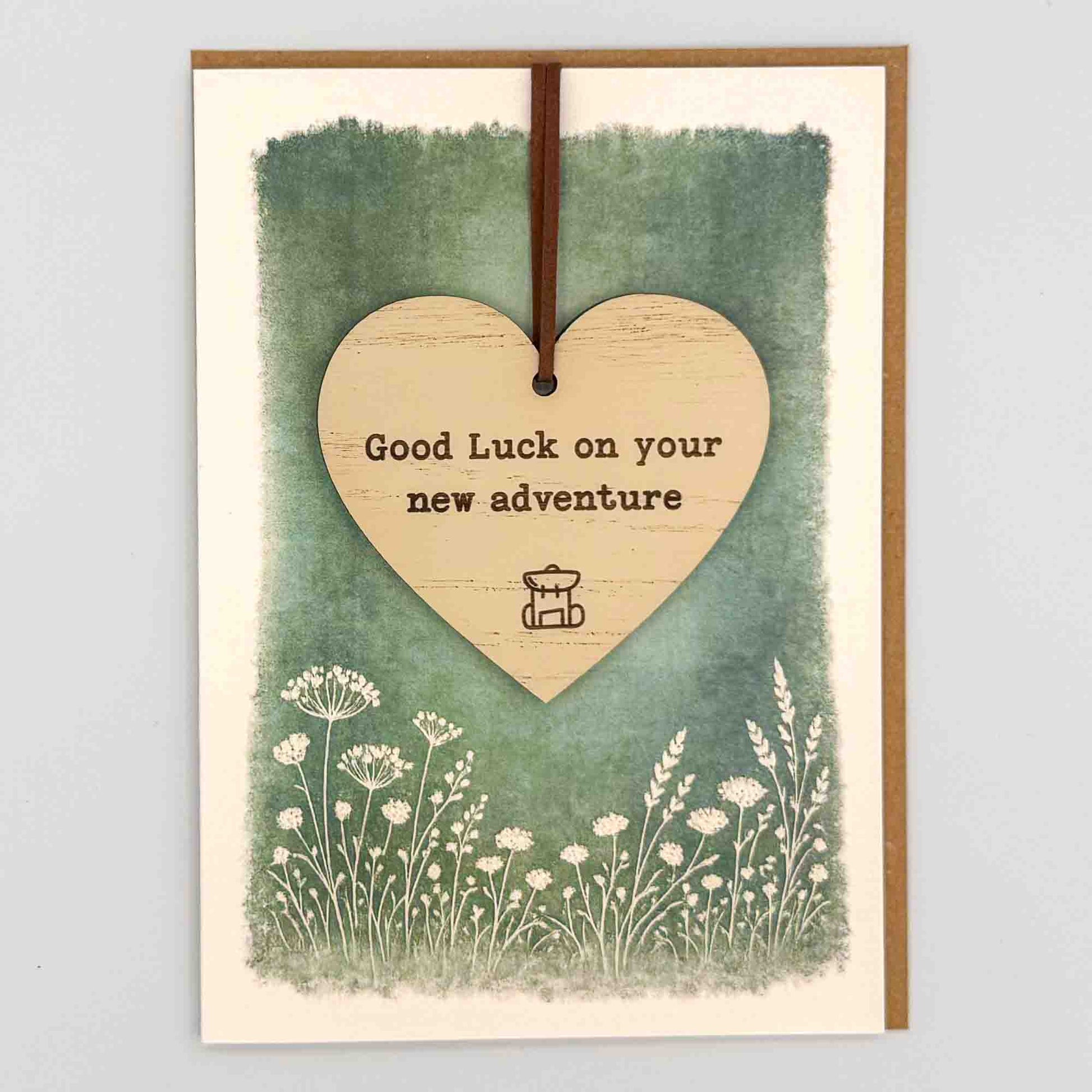 Good luck new adventure heart keepsake card from Sprinkled with Magic, featuring a removable wooden heart keepsake, rucksack icon, green botanical design and recycled kraft envelope.