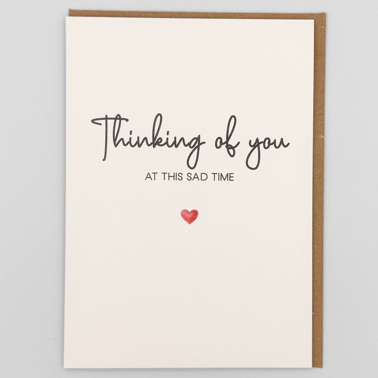 Thinking of you sympathy card from Sprinkled with Magic, featuring at this sad time wording, handwritten-style text, a small red heart and recycled kraft envelope.