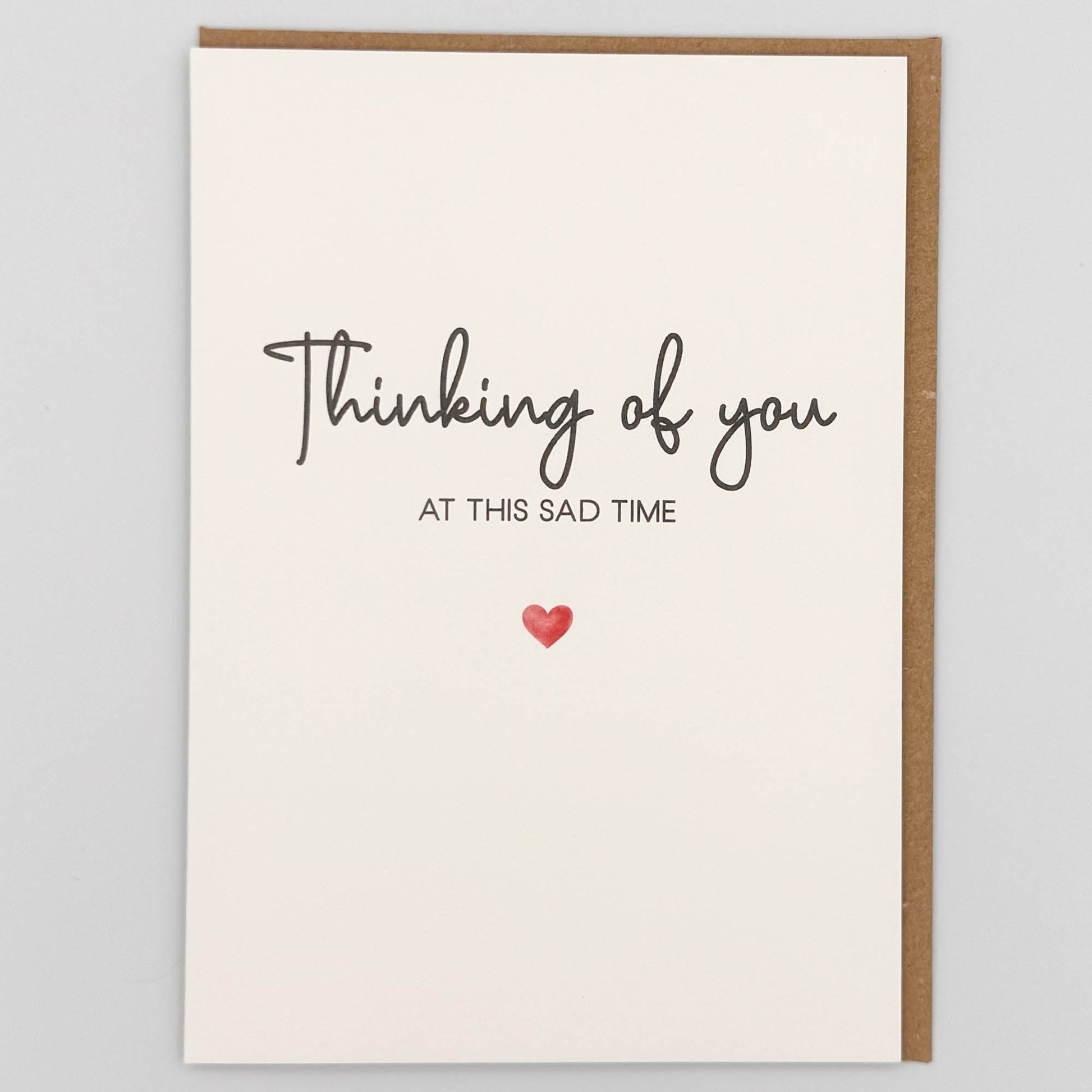 Thinking of you sympathy card from Sprinkled with Magic, featuring at this sad time wording, handwritten-style text, a small red heart and recycled kraft envelope.