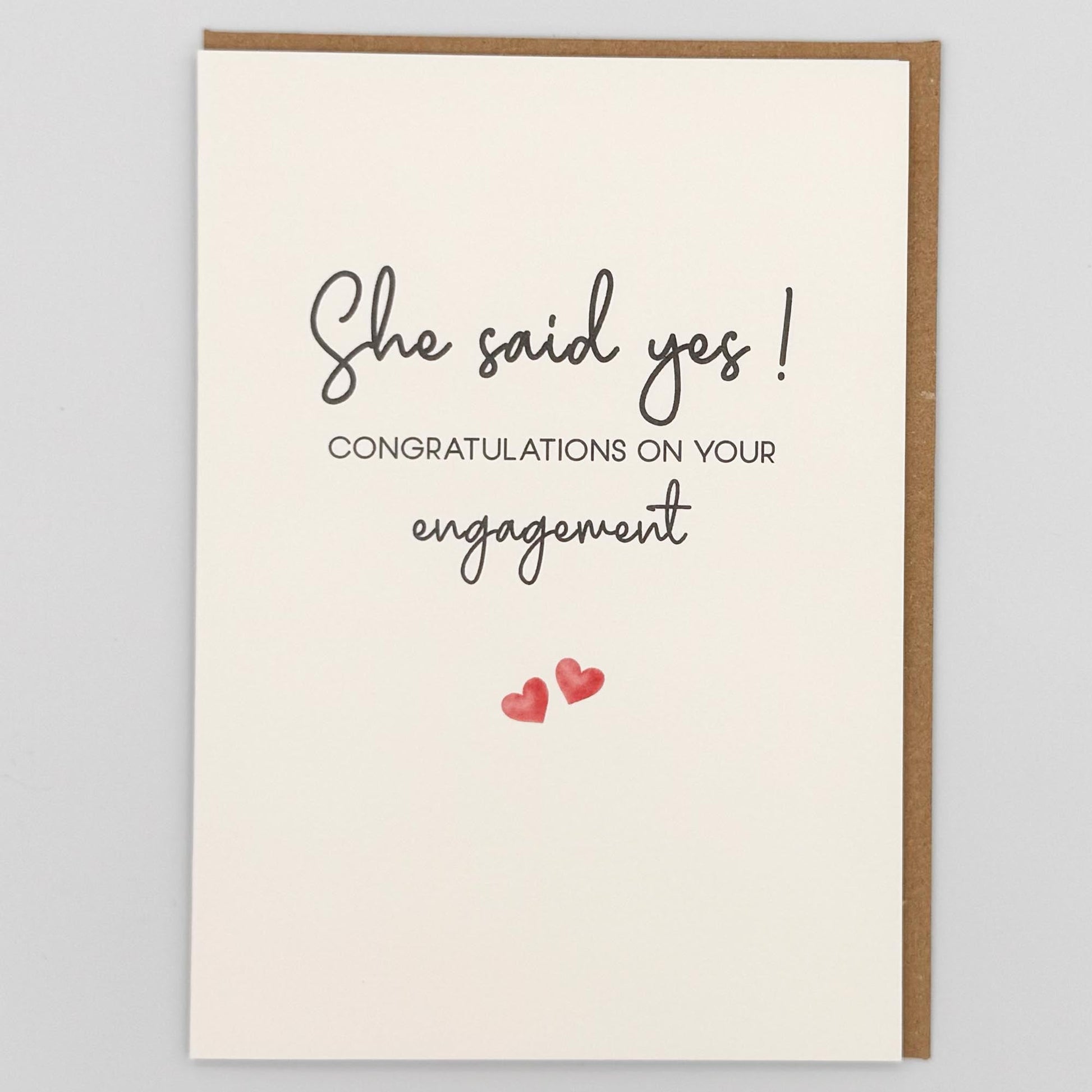 She said yes engagement card from Sprinkled with Magic, featuring handwritten-style engagement wording, two small pink hearts and recycled kraft envelope.