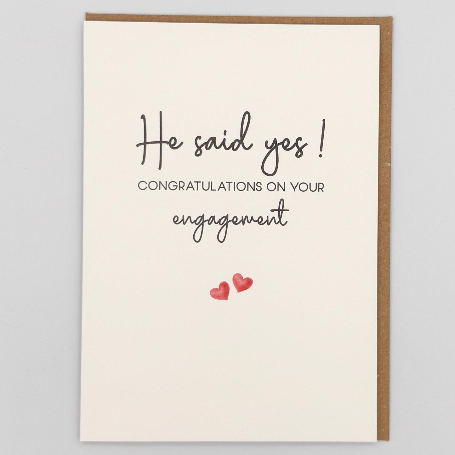 He said yes engagement card from Sprinkled with Magic, featuring handwritten-style engagement wording, two small pink hearts and recycled kraft envelope.