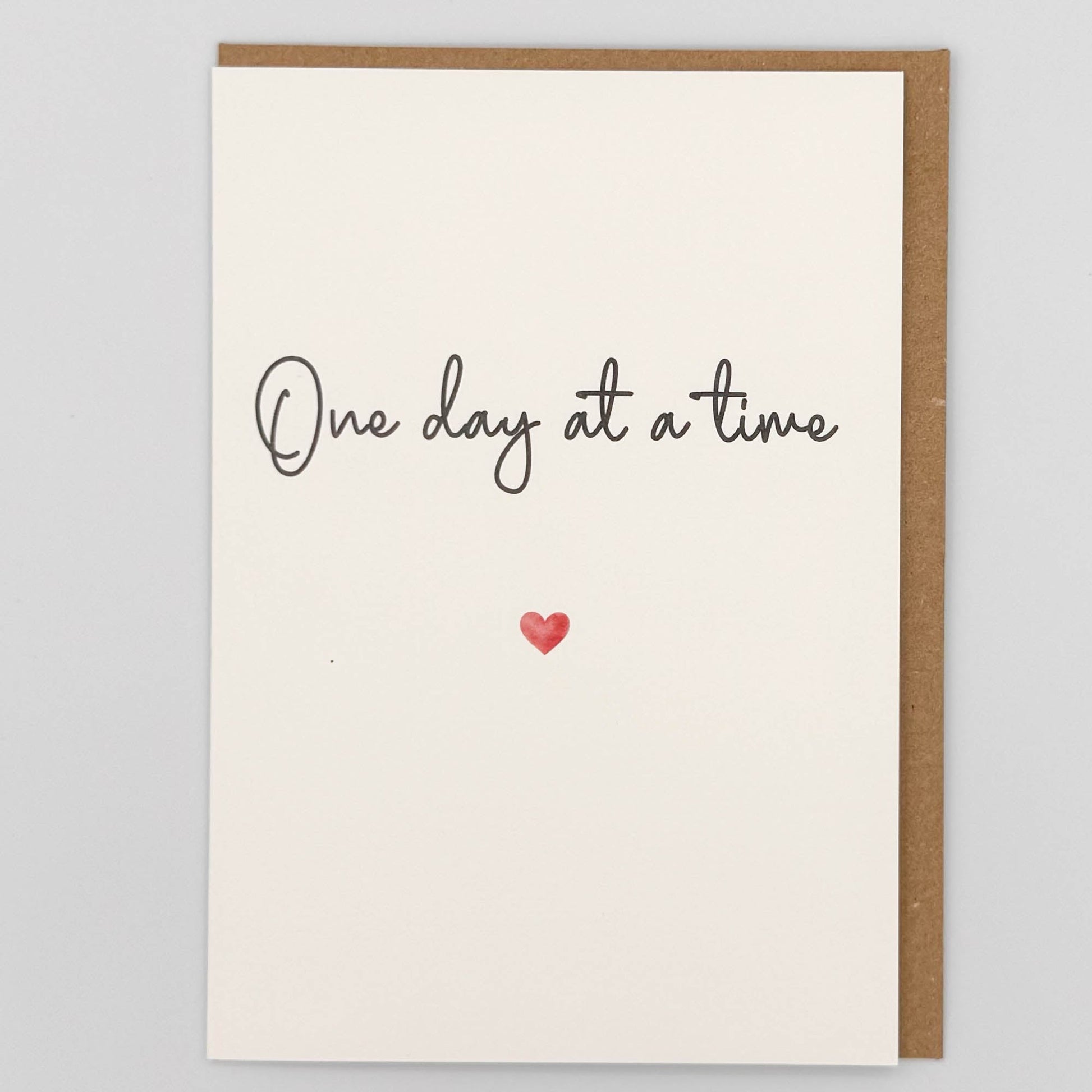 One day at a time card from Sprinkled with Magic, featuring handwritten-style reassurance wording, a small red heart and recycled kraft envelope.